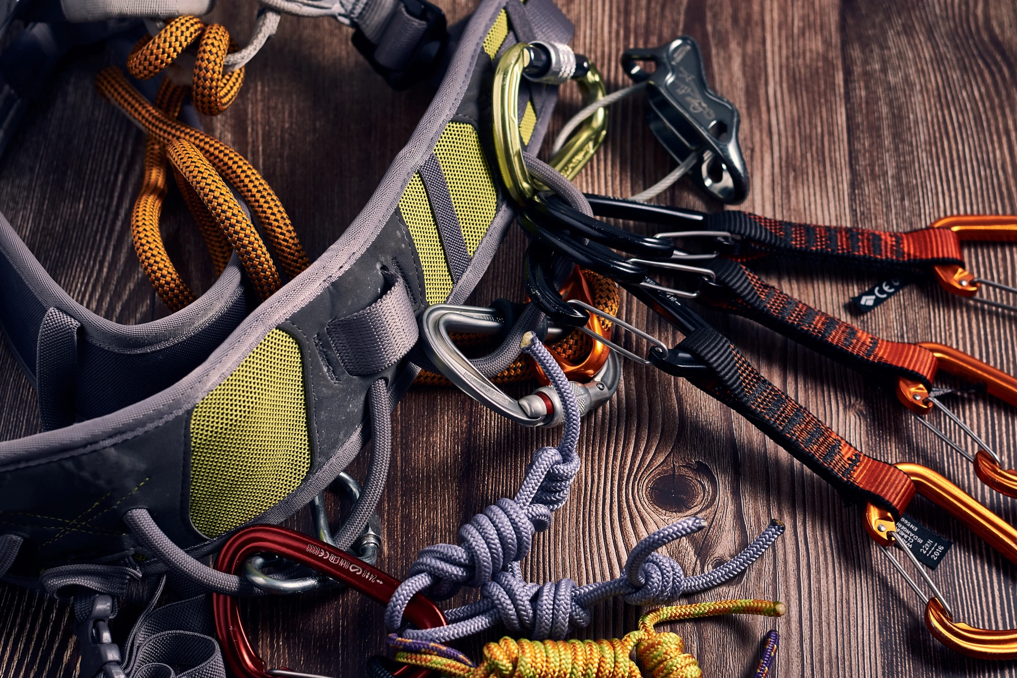 closeup-shot-many-colorful-climbing-carabiners-knots-wooden-surface